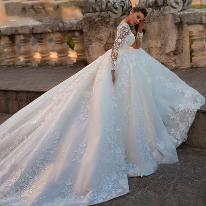 Woman in a white lace wedding dress standing in an outdoor setting with stone architecture.